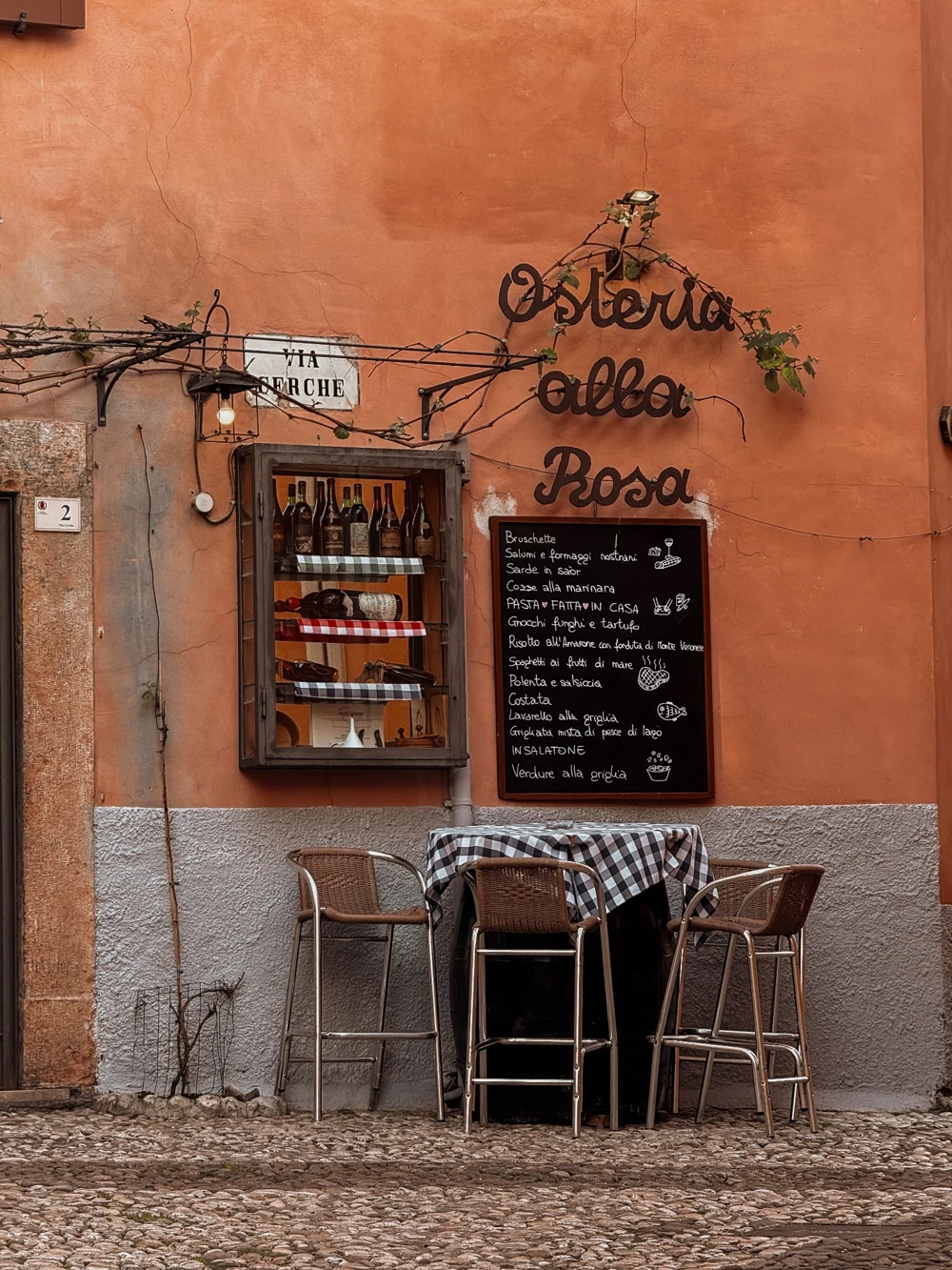 Façade d’une osteria, avec une ardoise de menu et des tables en terrasse